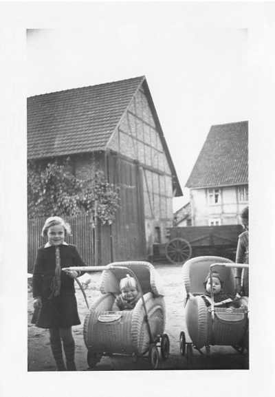 Schwarz-Weiß-Foto: Zwei Mädchen fahren zwei Kleinkinder in deren Kinderwagen aus. Das Kleinkind in dem Kinderwagen links bin ich. In dem Dorf Angerstein im Jahre 1954.