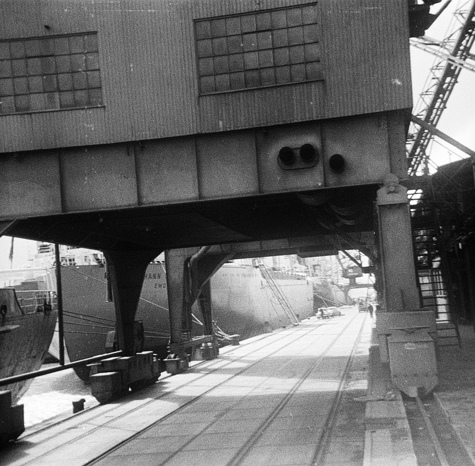 Blick unter einm großen Schiffskran hindurch auf VW-Käfer, die auf die MS Johann Schulte verladen und in die USA transportiert werden sollen. Die MS Johann Schulte mit Gangway. 1967. Foto: Erwin Thomasius.