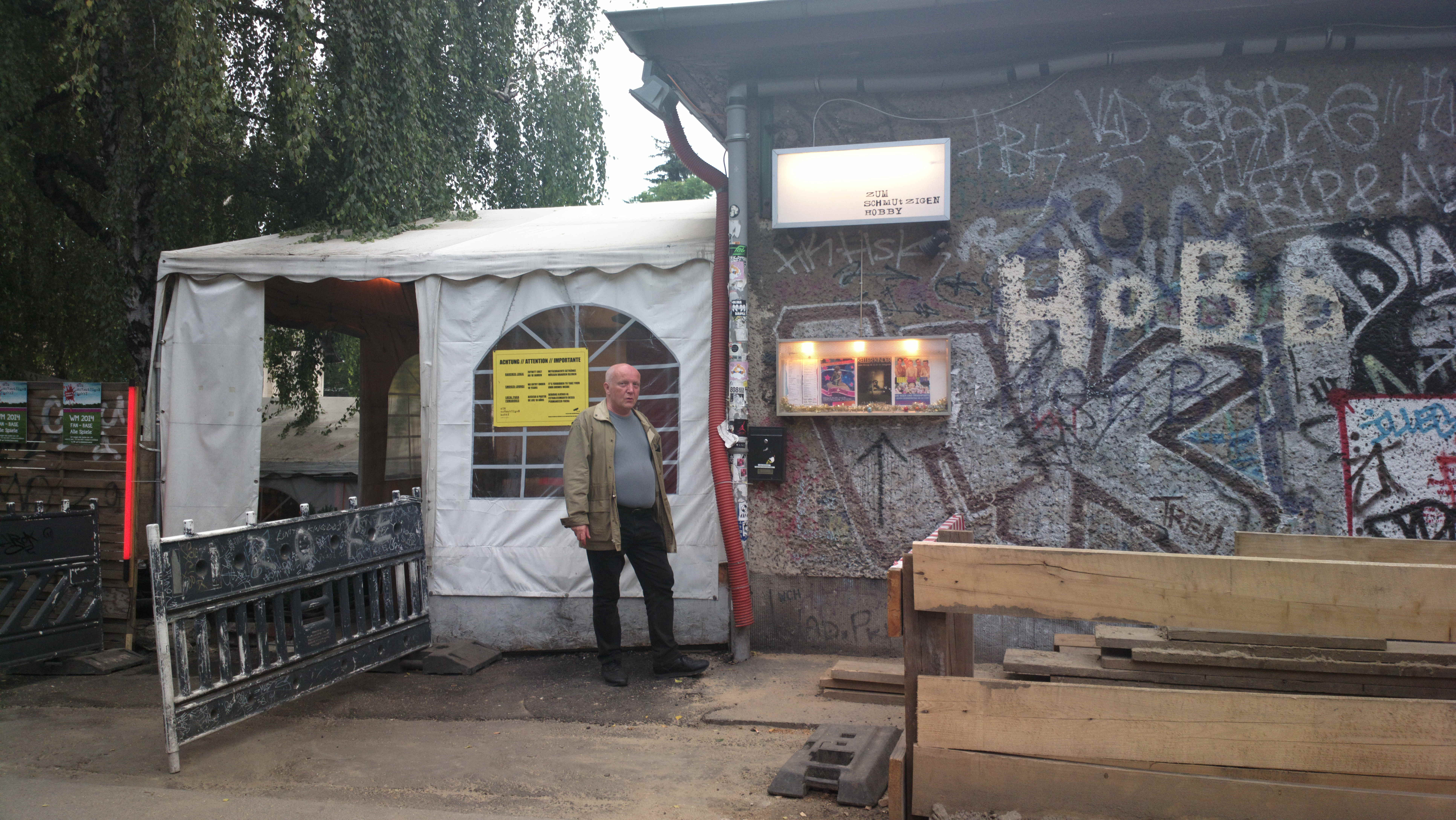 Farbfoto: Erwin Thomasius vor der Bar ZUM SCHMUTZIGEN HOBBY in dem alternativen Kulturzentrum RAW-Tempel in Friedrichshain in Berlin im Juni des Jahres 2014. Foto: Kim Hartley.